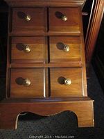 Close-up photo showing the front of the cherry chest with three drawers, each drawer having two brass knobs and a carved base.