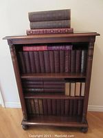 Front view of bookshelf filled with maroon-bound volumes and stacked books on top