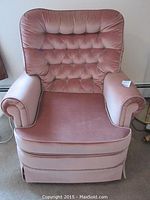 Front view of pink velvet tufted sitting chair with rolled arms and skirted base.
