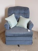 Front view of the blue upholstered chair with two light blue cushions, showing the tufted button backrest, padded arms and skirted base.