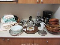 Photo of kitchen linens, knife racks, mixing bowls, kettle, coffee maker, toaster, wooden bowls varying sizes