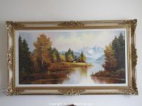 Front view of the large framed oil painting showing a lake, trees, mountains, and cottage in a natural landscape.
