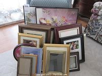 Initial overview of lot showing variety of picture frames and framed art prints stacked on floor.