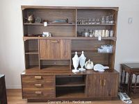 Front view of the large wood grain wall unit showing open shelves with glassware, closed cabinets, drawers, and decorative items placed on shelves.