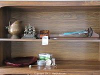 Shelf with assorted decorative items including brass copper pot, metal sailboat bookends, tortoiseshell styled box, glass candle holder, and a tray with glasses and a red wood tray below.