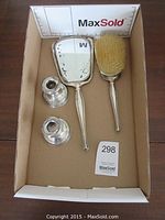 Photo showing sterling silver vanity set including hand-held mirror and brush along with two candlestick holders inside a box.