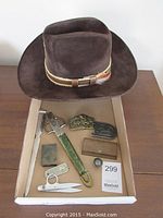 Photo showing the cowboy hat and all smaller items arranged inside a box including belt buckles, scissors, letter opener, and other small items.