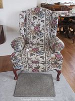 Front view of a floral theme wingback chair showing its patterned upholstery and wooden legs