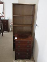 Front view of 5 drawer wood end table in front of bookcase, showing drawer pulls and top surface condition