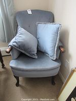 Blue wingback chair with two pillows placed on the seat, showing front view and upholstery details.