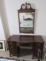 Photo of the dark wood vanity desk with seven drawers and integrated decorative scalloped edges and drawer pulls, positioned below the wall mirror.