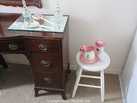 Wide shot of vanity items on mirrored tray and white stool with pink and white painted ceramic pieces
