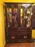 Full view of large dark wood Asian style hutch with four glass doors on top section, four wooden doors on bottom, and two drawers in between. Brass-toned decorative pulls and trim.