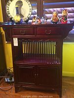 Front view of the shelving unit showing the two drawers at the top, an open shelf with vertical slats, and double-door cabinet below. Some items displayed on top but not included.