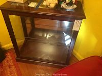 View of the wood and glass display case showing dark wood frame, glass shelf and solid top surface from front angle.