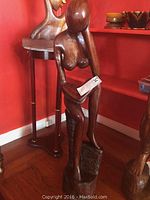 Front view of full carved wooden statue of a seated nude woman reading