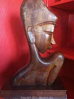 Side profile of the wood carved woman bust showing detailed facial features and smooth finish against a red background.