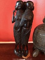 Frontal view of the three carved African women figures in dark wood showing the details of their posture and necklaces.
