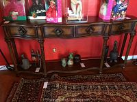 Front view of wood console table with four drawers and decorative turned legs, showing several collectible items on top and bottom shelf removed from lot