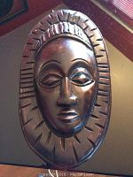 Front view of dark wood carved African mask with smooth finish and sunburst pattern border.
