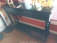 View of the front of the wood console table showing the top surface with dents and decorative apron.