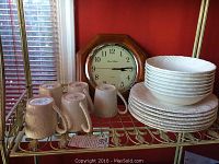 Photo of 6 mugs, stacked plates and bowls, and wooden-framed clock on a metal shelf