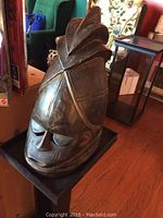 Side angled view of carved wooden African mask on wooden stand, showing detailed carving and dark wood finish.