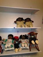 Overall view showing six Cabbage Patch Kids dolls displayed on shelves, four seated in doll chairs, two standing/sitting on shelf. Various outfits and poses.