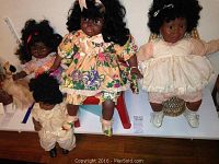 Four vinyl dolls seated and standing with varying clothing and hairstyles, also includes a beige dog toy visible on left corner. Highlighting the variety and condition of dolls.