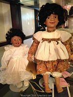 Two dolls displayed, Moments Treasured Tabitha in white lace dress and smaller, Seymour Mann Amber larger with patterned dress and charms, both with curly black hair and tags