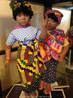 Two William Tung porcelain dolls dressed in colorful traditional attire, standing on white stands with Certificates of Authenticity visible below.