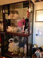 Full view of both top and bottom wooden and glass display cabinets showing dolls inside the glass cabinets.