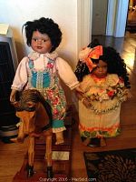 Photo showing two porcelain dolls and a wooden rocking horse together, the dolls are dressed in colorful dresses and have black curly hair.