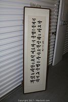 Full length image of framed Asian calligraphy scroll with black characters on white background and brown frame