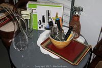 Overview of lot showing glass carafes, ceramic tray, yellow bowl with bar accessories, and new in box wine opener.