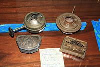 Photo showing two metal kerosene burners and two decorative metal trinket boxes on a wooden surface