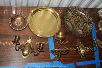 Photo showing two hammered brass chargers, Hebrew Seder dish, candle sconces, brass cup and soap holder on wooden surface.