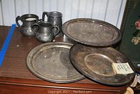 Silver plate serving trays, two sugar bowls, and a tankard arranged on a wooden surface showing all items