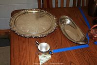 Photo shows two large silverplate trays and a silver sugar bowl on a wooden table with blue tape outline