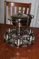Full view of vintage silver toned fondue set with pot, lid, burner stand, tray and six small bowls arranged around the tray.