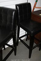 Set of two black faux leather bar stools showing front and side view, highlighting condition and structure.