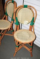 Two caned seat rattan bistro chairs placed side by side with visible green accents on the frame.