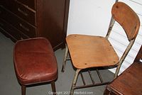 Photo of old wooden school chair with metal legs alongside mid century vinyl stool, showing wear and condition.