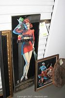 Framed colorful John Alvin Filmex '76 pin-up girl poster leaning against white wall in storage unit