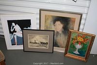 Four framed artworks arranged on floor: an original flower painting in gold frame, a signed etching of Danish landscape, abstract print of a seated woman, pastel portrait print.