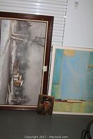 All three art pieces shown side by side: large snowscape, abstract print, and small portrait leaning against the wall
