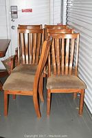 Six wooden dining chairs grouped together, showing front and side views. Two chairs have armrests; four are armless. Upholstered fabric seats show discoloration and some wear. Wood frames have minor scratches.