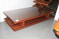 Full view of rectangular walnut veneer coffee table with glass top cover on a concrete floor.