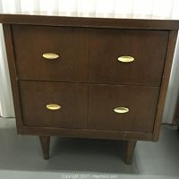 Front view of the night stand showing wood veneer surface, tapered legs, and gold tone cat's eye handles on two drawers.