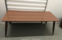 Full view of mid-century modern coffee table with wood grain laminate top and tapered wooden legs with metal caps.